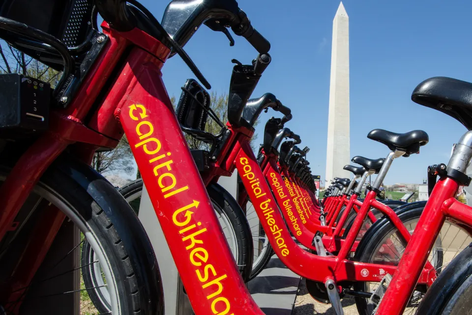 Close-up of red Capital Bikeshare bikes with Washington Monument in background.
